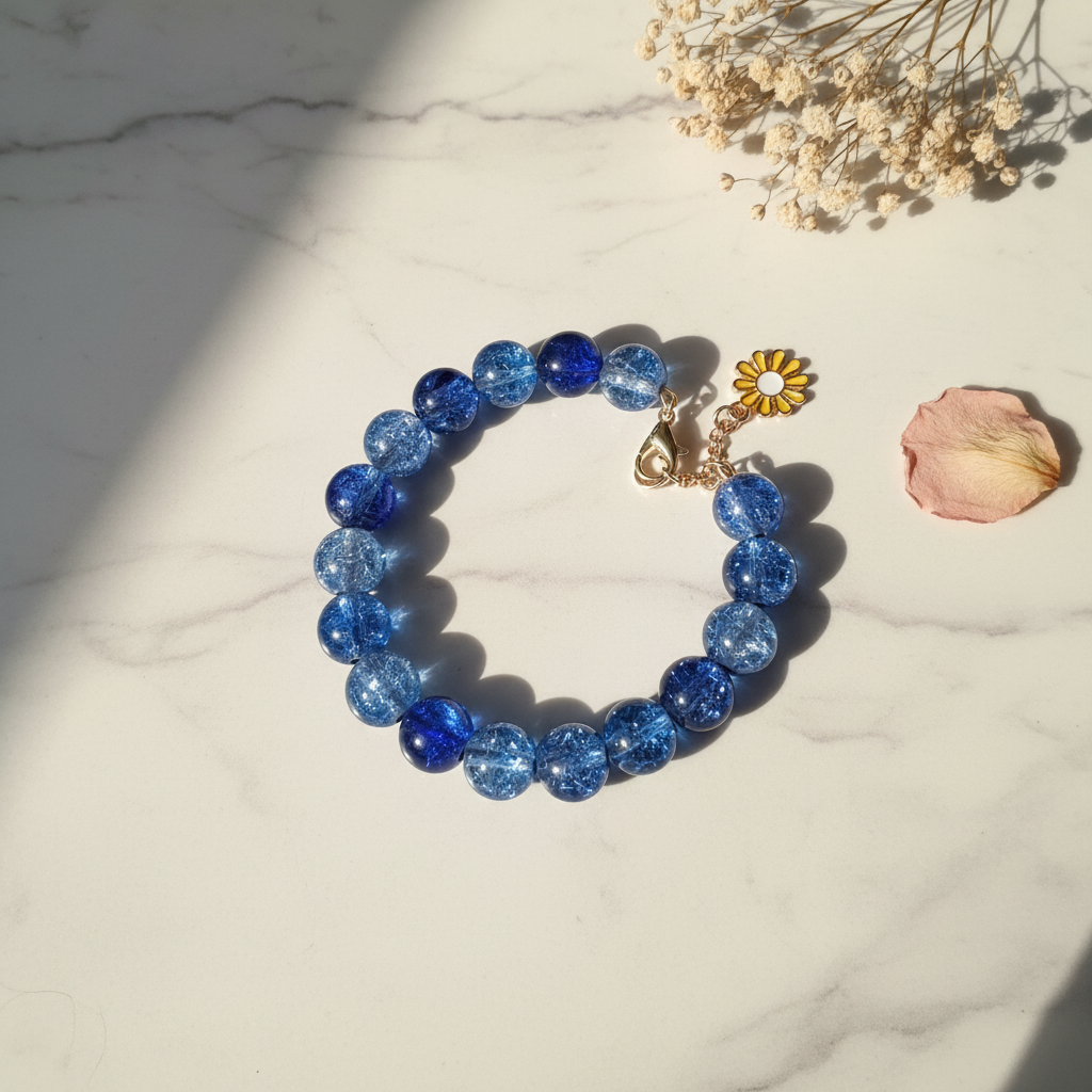 Blue crackle glass bead bracelet with yellow daisy charm on marble lifestyle