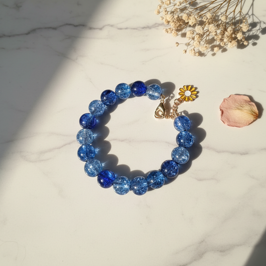 Blue crackle glass bead bracelet with yellow daisy charm on marble lifestyle