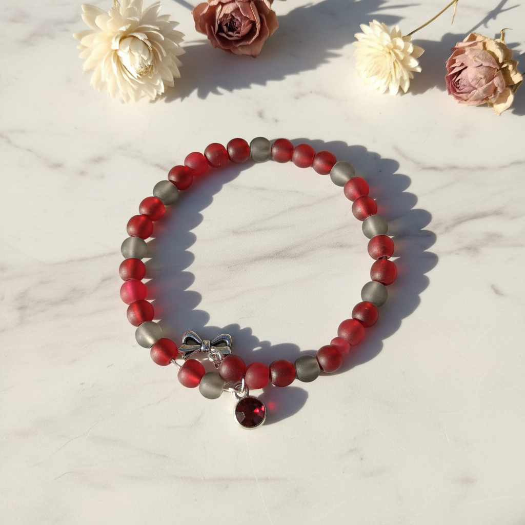 Frosted red and gray glass moon bead memory wire wrap bracelet with bow and red crystal charm on marble lifestyle