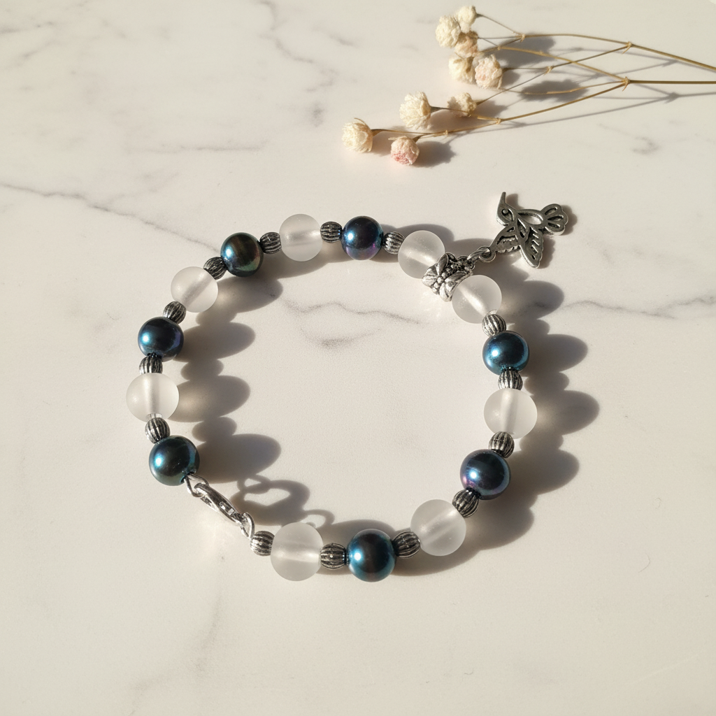 Dark pearl and frosted glass moon bead bracelet with silver hummingbird charm on marble lifestyle background