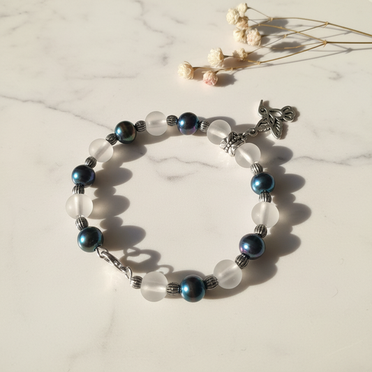 Dark pearl and frosted glass moon bead bracelet with silver hummingbird charm on marble lifestyle background
