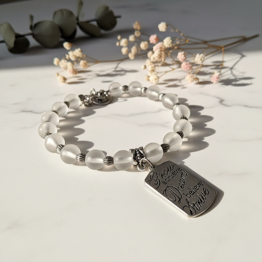 Frosted white glass moon bead bracelet with inspirational silver tag charm on marble lifestyle background