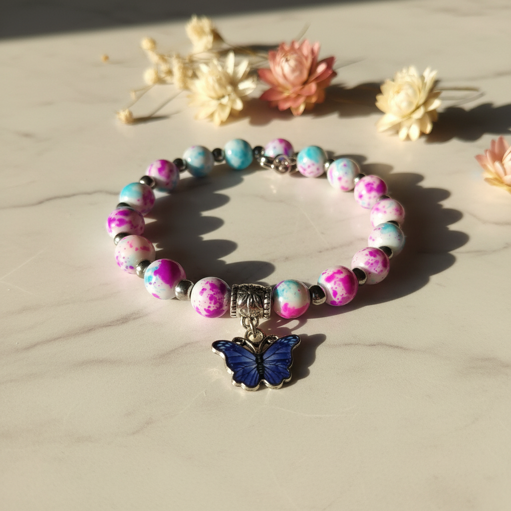 Pink and teal splatter bead bracelet with blue butterfly charm on marble lifestyle background